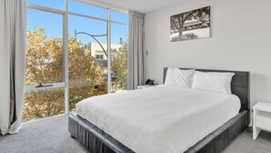 A bedroom with a large bed, a bedside table, a nightstand, a window with curtains, and a wall-mounted picture. - Mawson Lakes Hotel & Function Centre (Mawson Lakes)