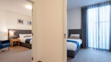 Una habitación de hotel con dos camas, un escritorio, una silla y un amplio ventanal con cortinas.