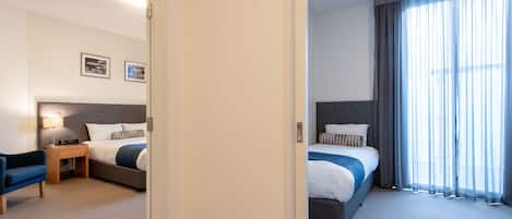 A hotel room with two beds, a desk, a chair, and a large window with curtains.