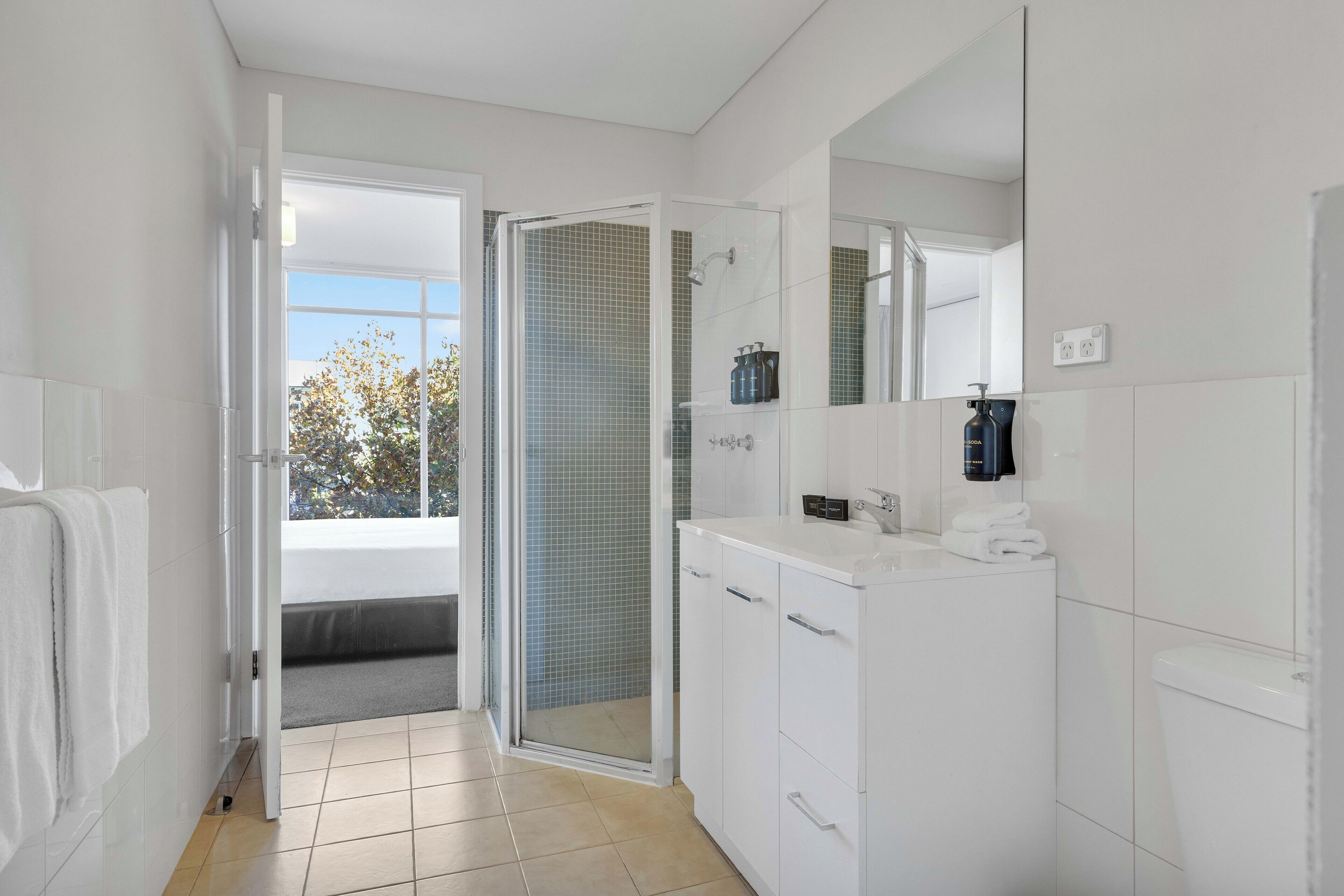 Une salle de bain moderne équipée d’une douche, de toilettes et d’un lavabo, avec un grand miroir et une vue sur l’extérieur.