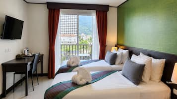 Habitación de hotel con dos camas, un escritorio, un televisor y un balcón con vistas a edificios.