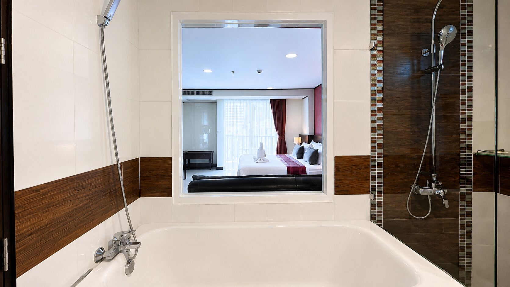 Ein modernes Badezimmer mit einer großen Badewanne, einer Duschkabine und einem Fenster mit Blick auf ein Schlafzimmer.