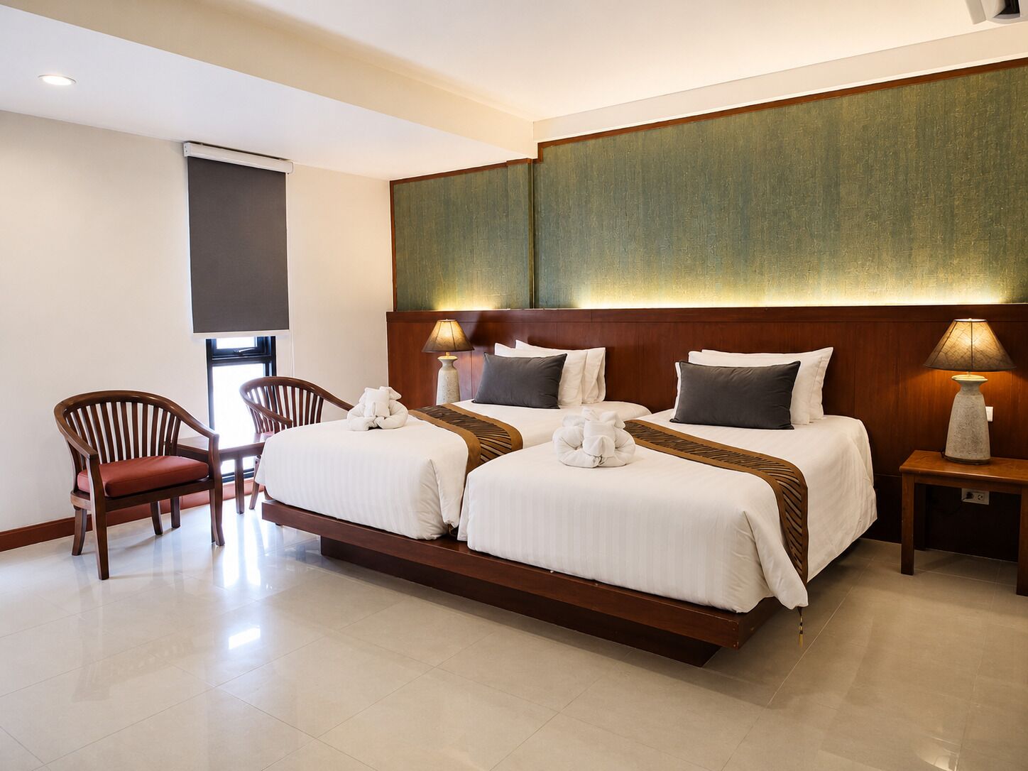 Quarto de hotel com duas camas, uma cadeira, mesa de cabeceira e TV fixada na parede.