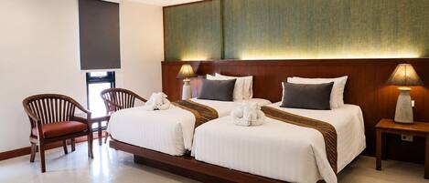Quarto de hotel com duas camas, uma cadeira, mesa de cabeceira e TV fixada na parede.