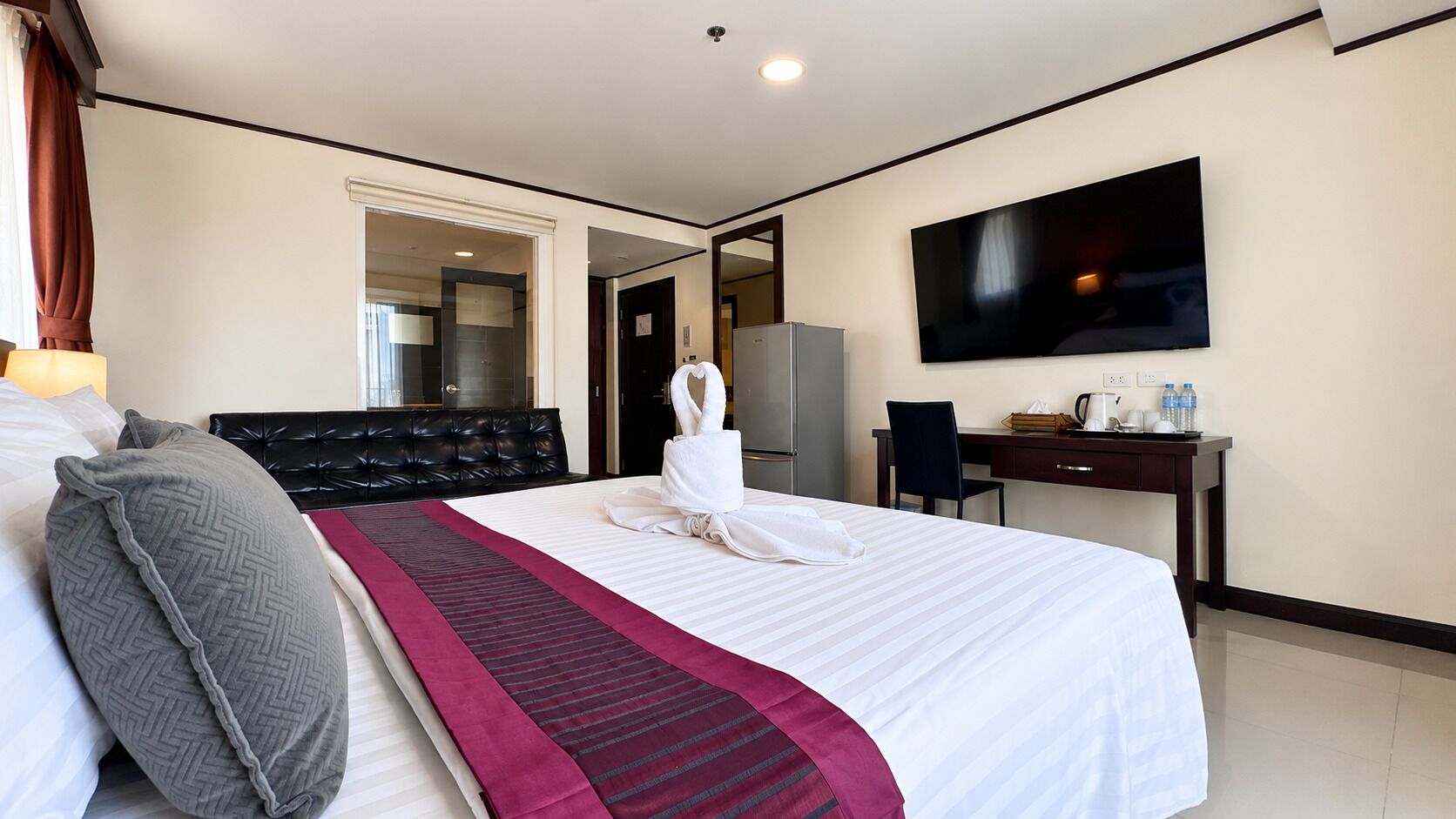 Habitación de hotel con cama, escritorio, televisión y baño visible a través de una puerta abierta.