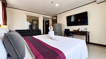 Habitación de hotel con cama, escritorio, televisión y baño visible a través de una puerta abierta.