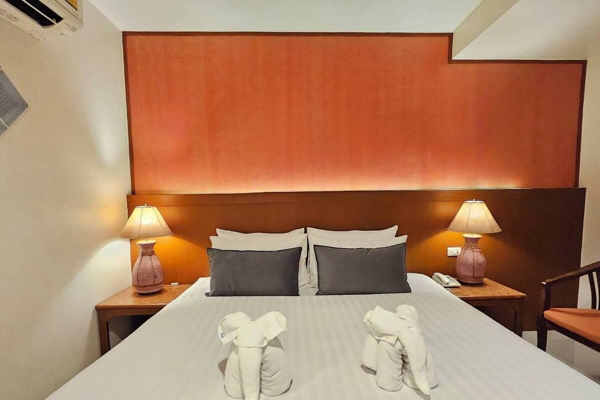 Et hotelværelse med en stor seng, to sengeborde med lamper, et træhovedgærde og to håndklæder på sengen.