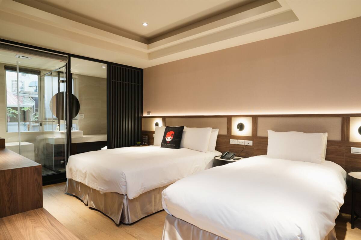 A hotel room with two beds, a desk, and a glass door leading to a balcony.