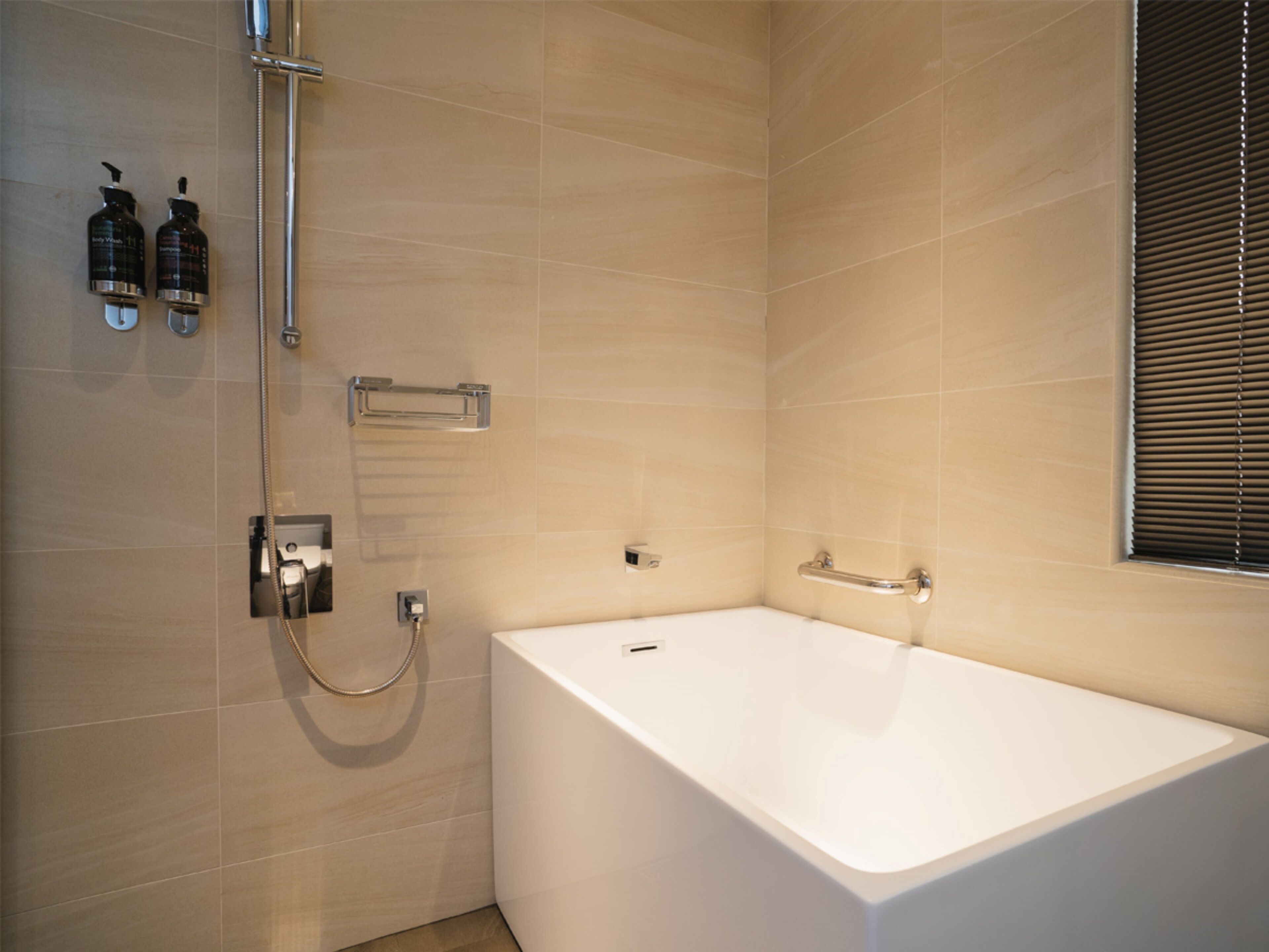 Un baño moderno con una bañera blanca, un cabezal de ducha manual y dos botellas de champú en la pared.