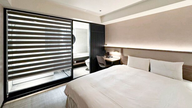 Quarto de hotel moderno com uma cama grande, uma mesa de trabalho e uma porta de vidro deslizante.