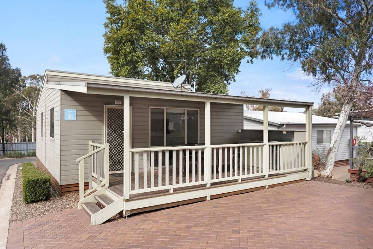 A single-story mobile home with a covered porch, a satellite dish, and a brick driveway.