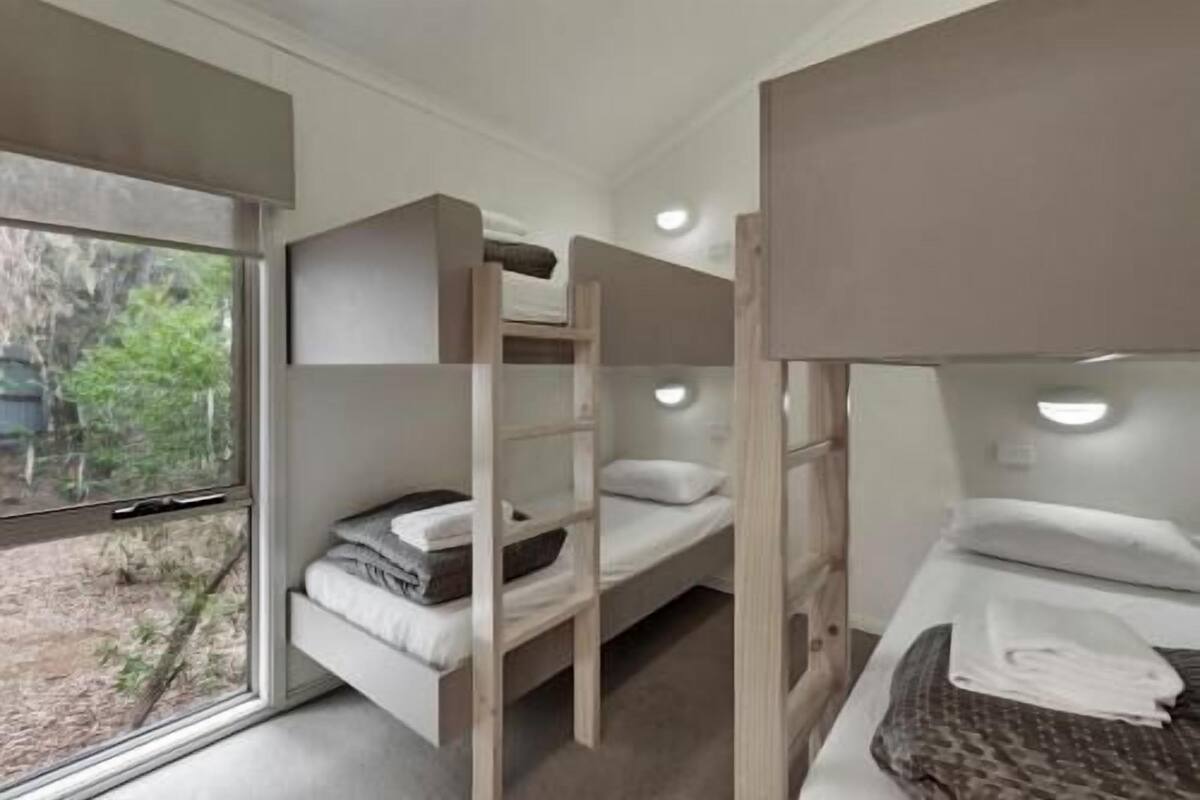 A room with bunk beds, a window with a view of greenery, and a door.