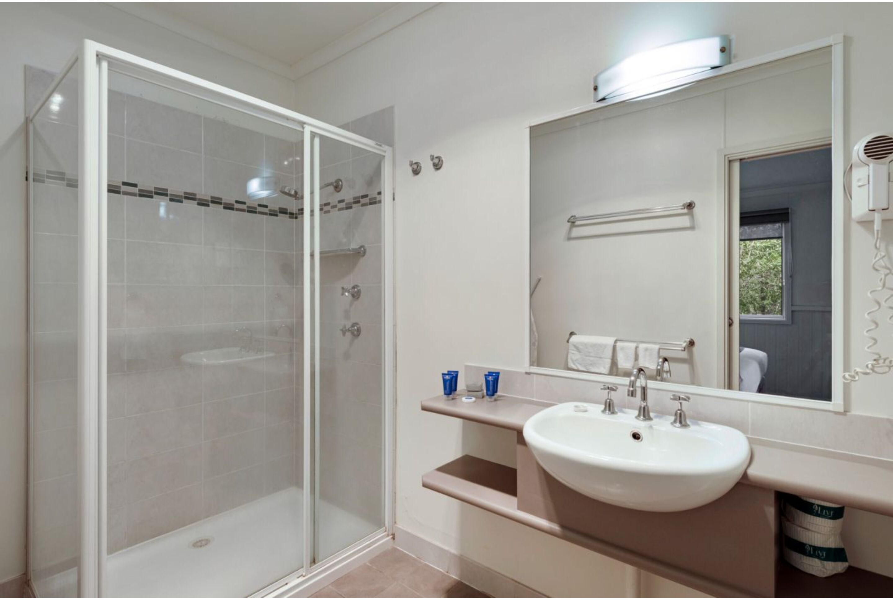 A modern bathroom with a glass-enclosed shower, a white sink, and a large mirror.