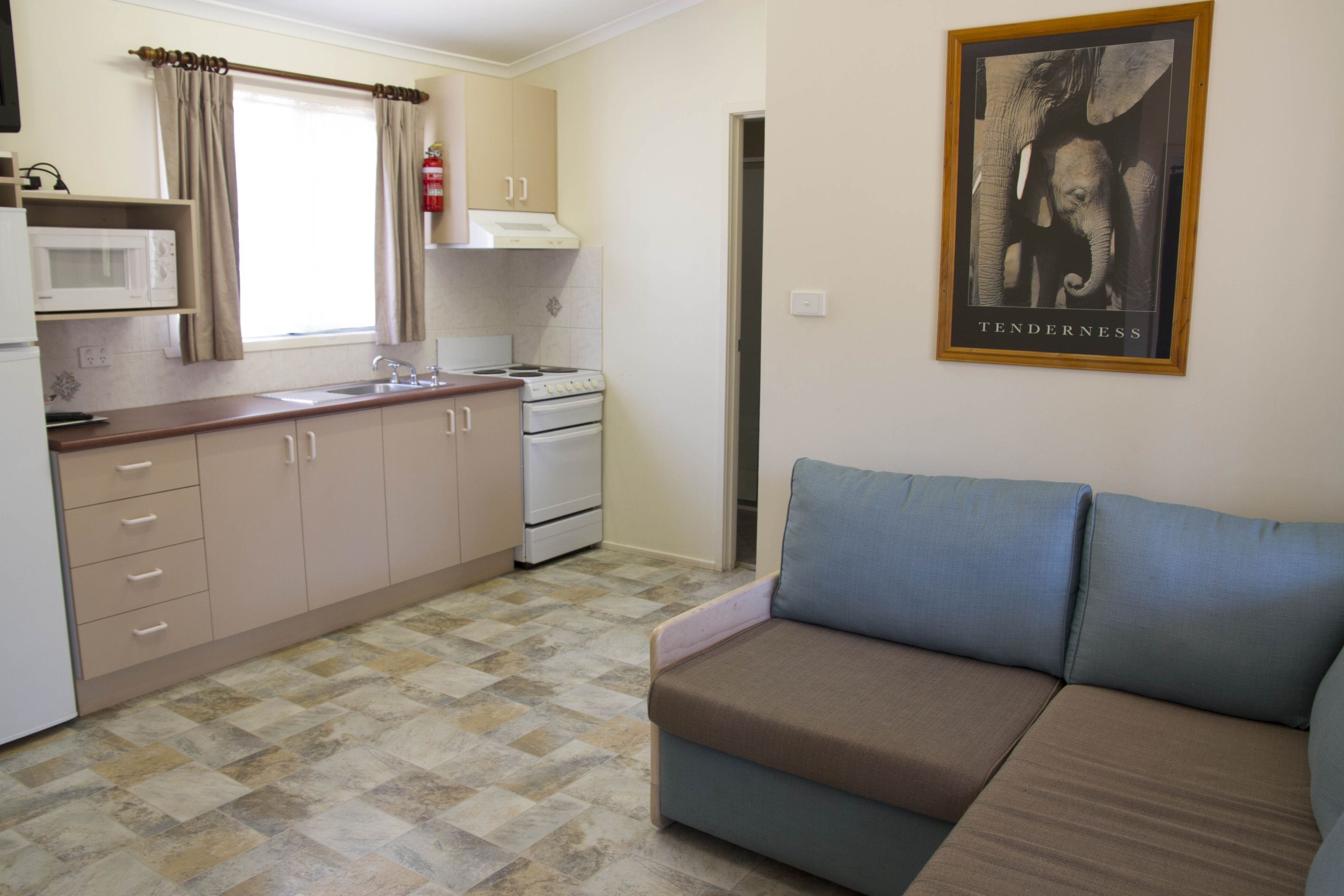 A compact kitchen with a microwave, stove, and cabinets. There is a sofa and a framed picture on the wall.