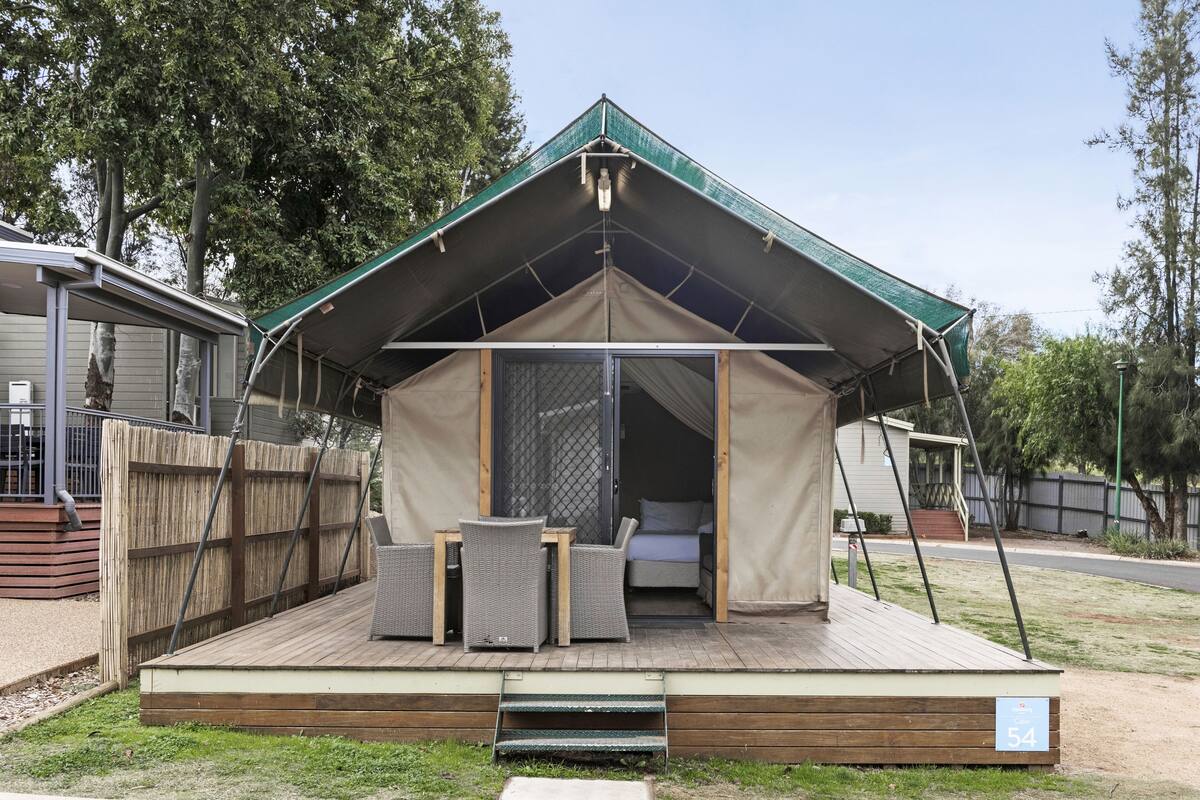 A single-story tent with a green roof, a wooden deck, and a small outdoor seating area with two chairs and a table.