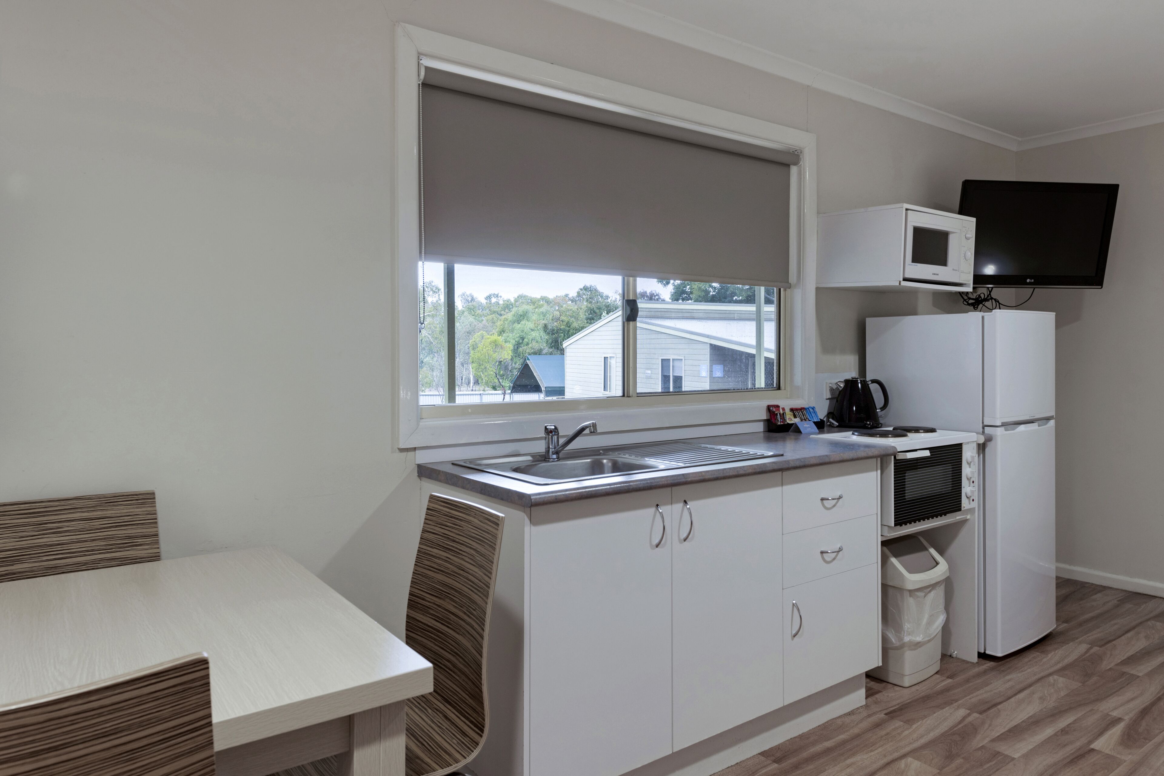 Una cocina compacta con ventana, microondas, refrigerador y lavamanos.