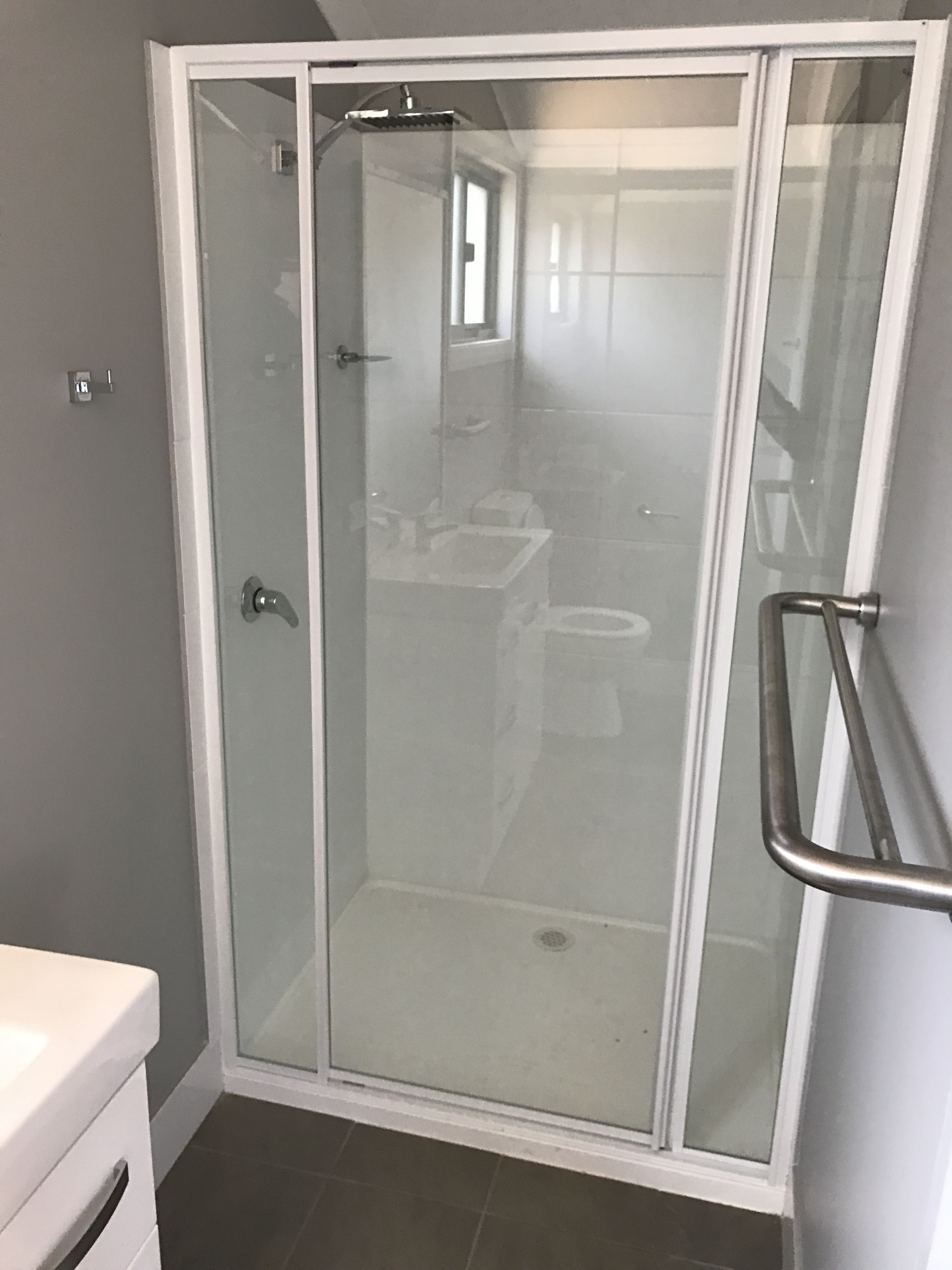 A glass-enclosed shower with a white frame, a white sink, and a toilet visible through the glass.