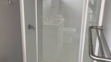 A glass-enclosed shower with a white frame, a white sink, and a toilet visible through the glass.