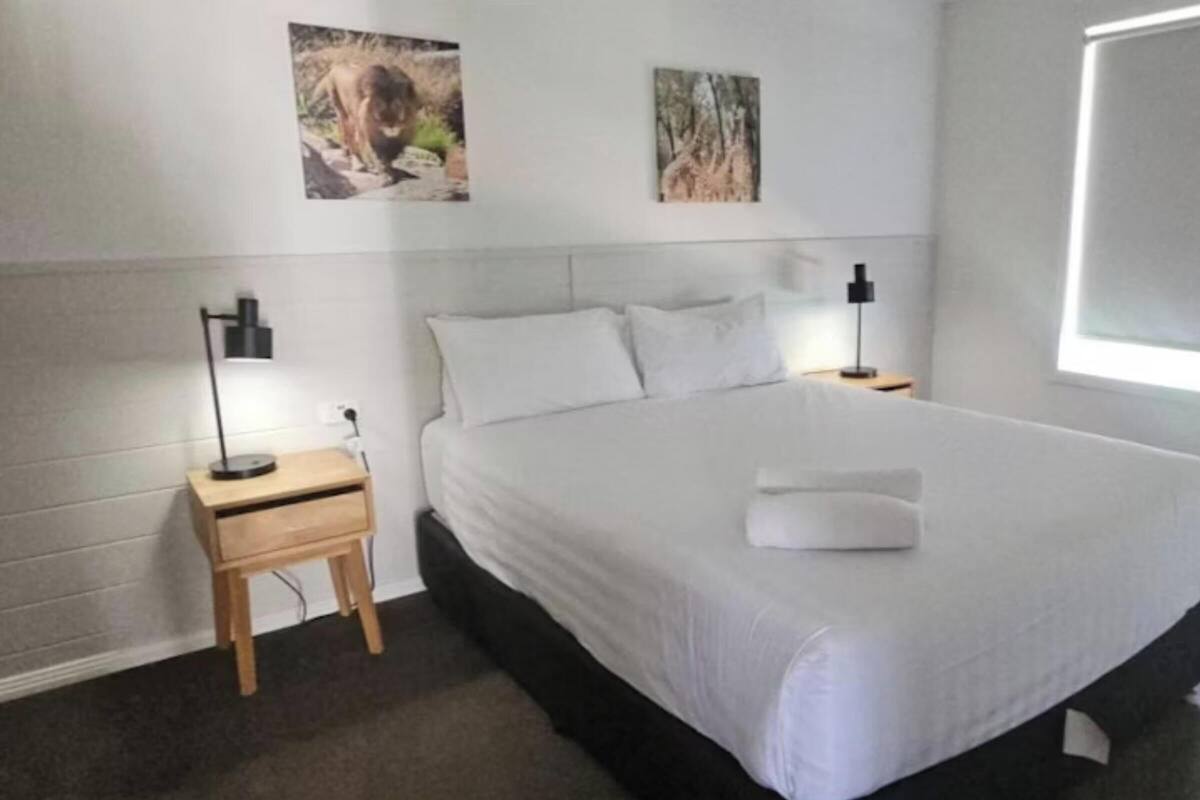 A neatly made bed with white linens and a folded towel, two bedside lamps, and two framed pictures on the wall.