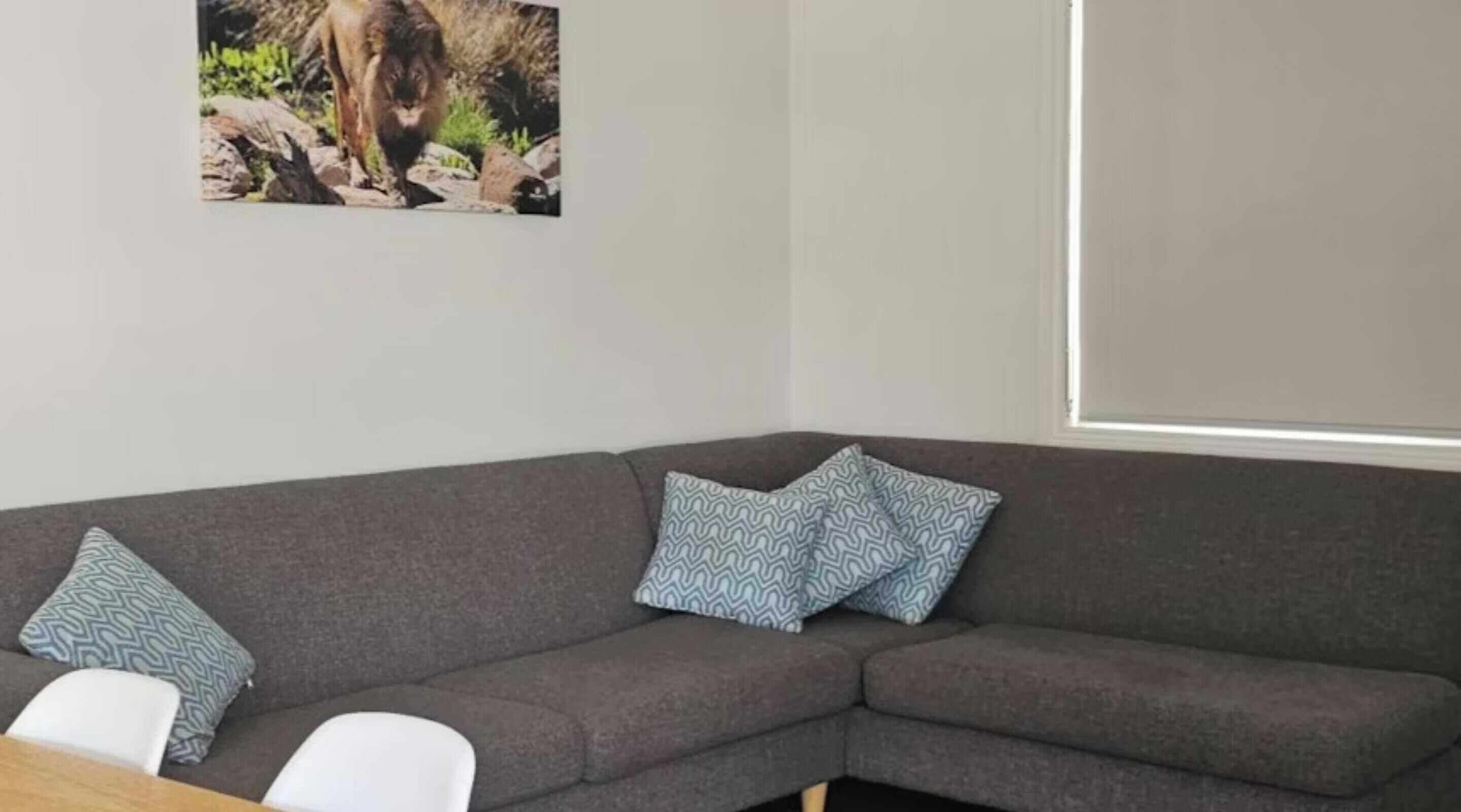 Un sofá gris con almohadones estampados, una silla blanca y un cuadro con un león en la pared.