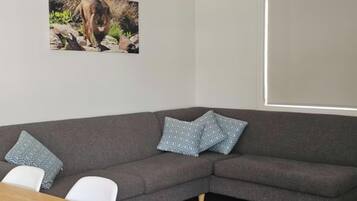 Un sofá gris con almohadones estampados, una silla blanca y un cuadro con un león en la pared.
