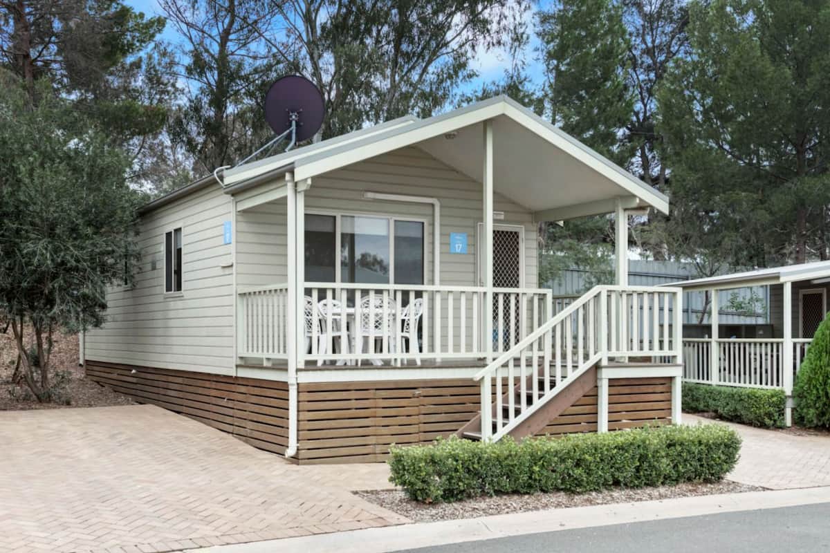 A single-story mobile home with a covered porch, a satellite dish, and a number '17' sign.