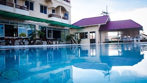 Una piscina con agua cristalina, rodeada por un edificio con techo morado y toldo verde.