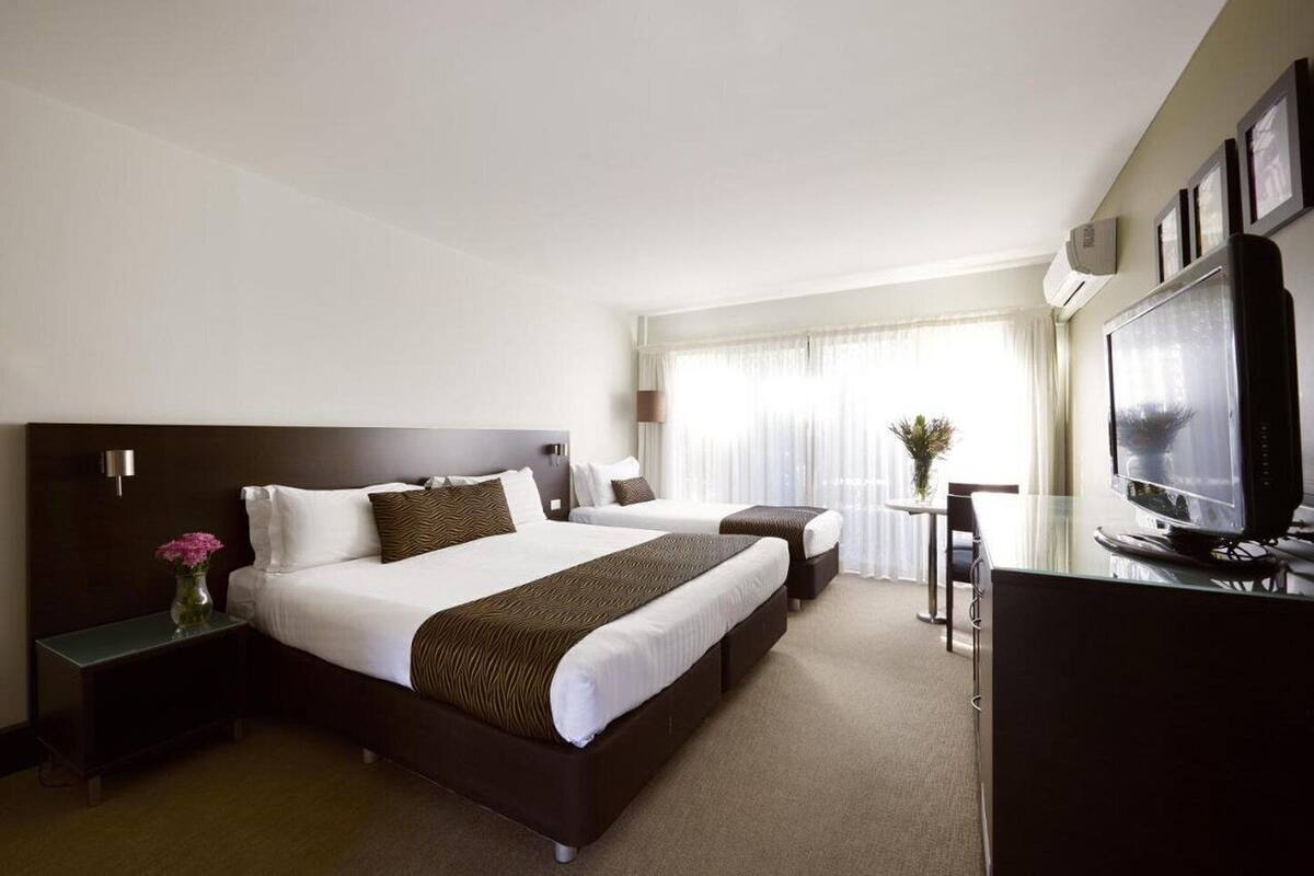 A hotel room with a large bed, a smaller bed, a desk with a TV, and a window with curtains.