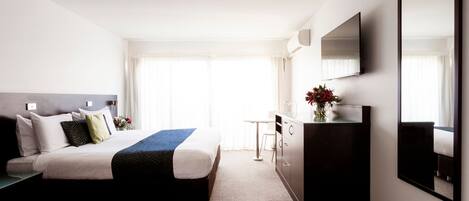 A hotel room with a bed, a desk, a chair, a dresser, and a large mirror.