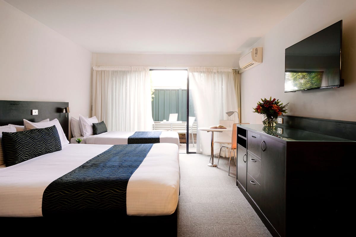 A hotel room with two beds, a desk, a chair, a TV, and a view of the outdoors.