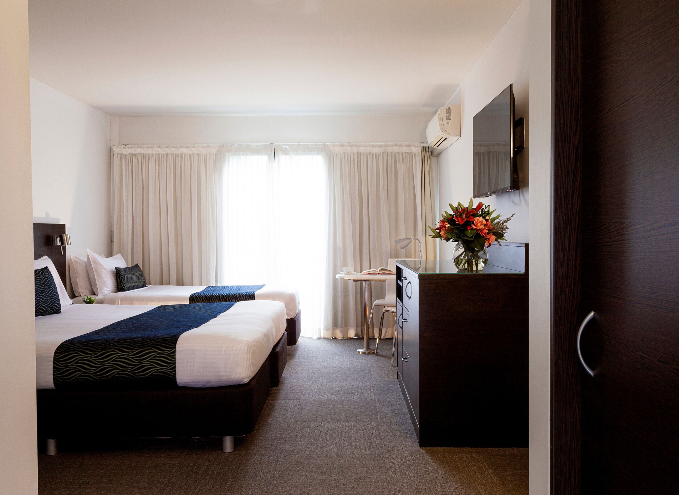 Hotelkamer met twee bedden, een bureau, een stoel, een dressoir, een spiegel en een raam met gordijnen.
