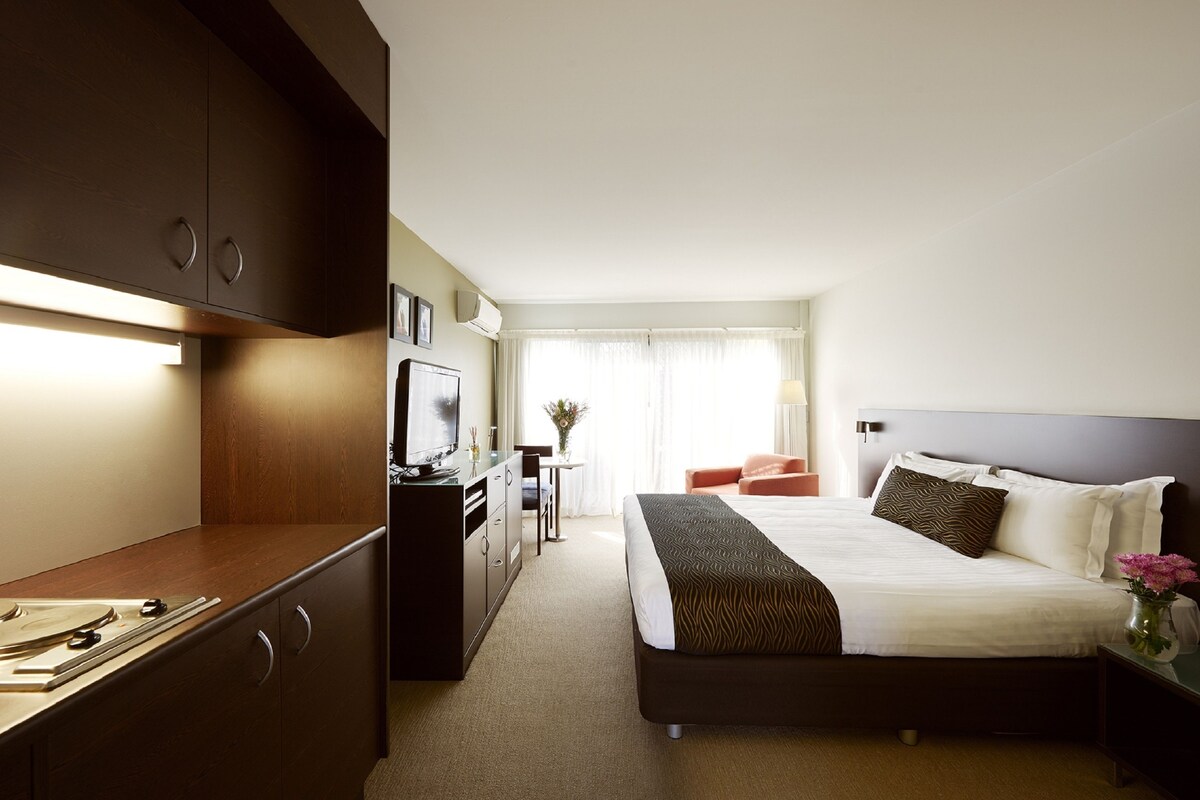 A hotel room with a bed, a desk, a television, and a window with curtains.