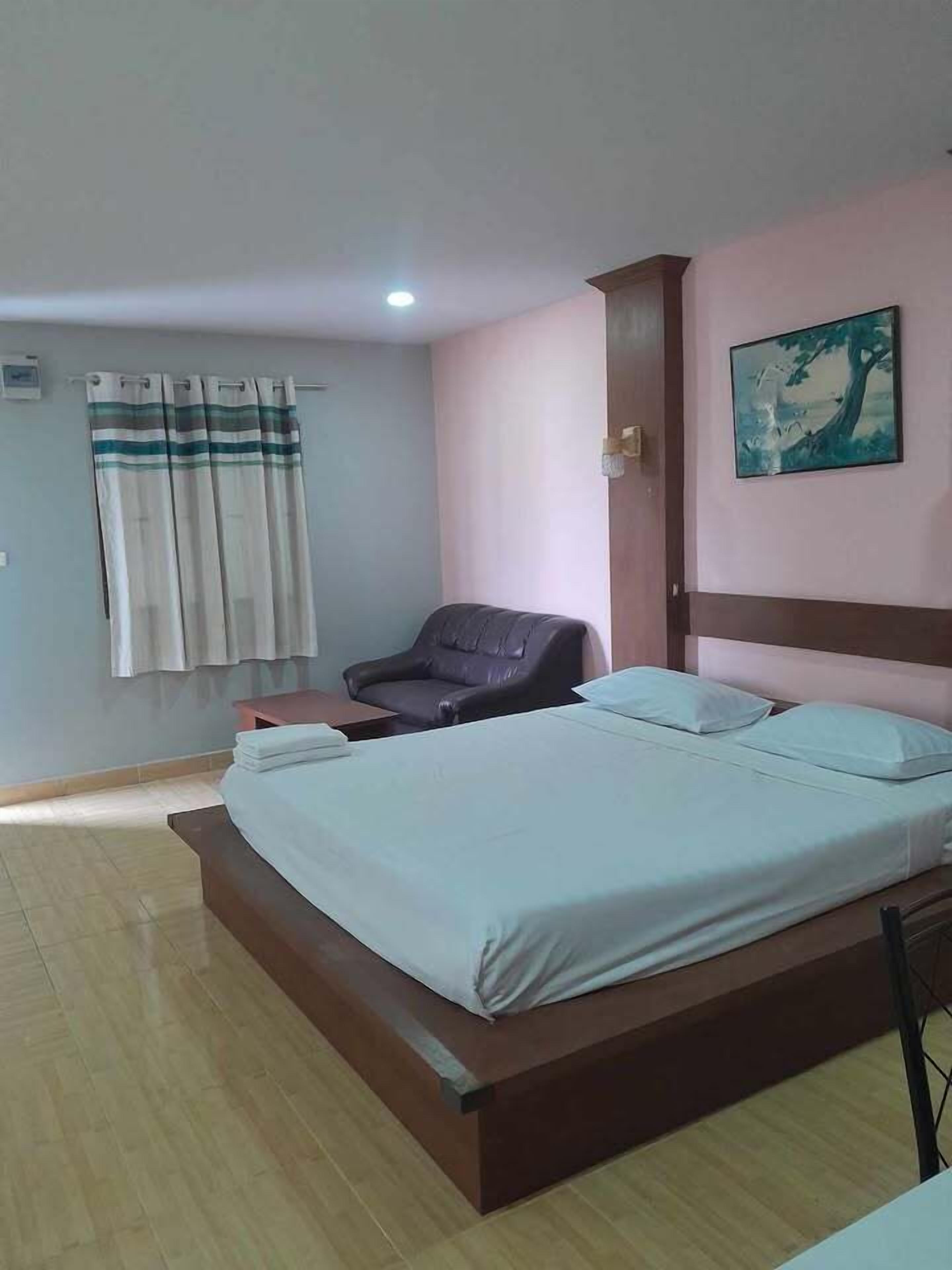 Un dormitorio con cama, una silla, un cuadro y una cortina.