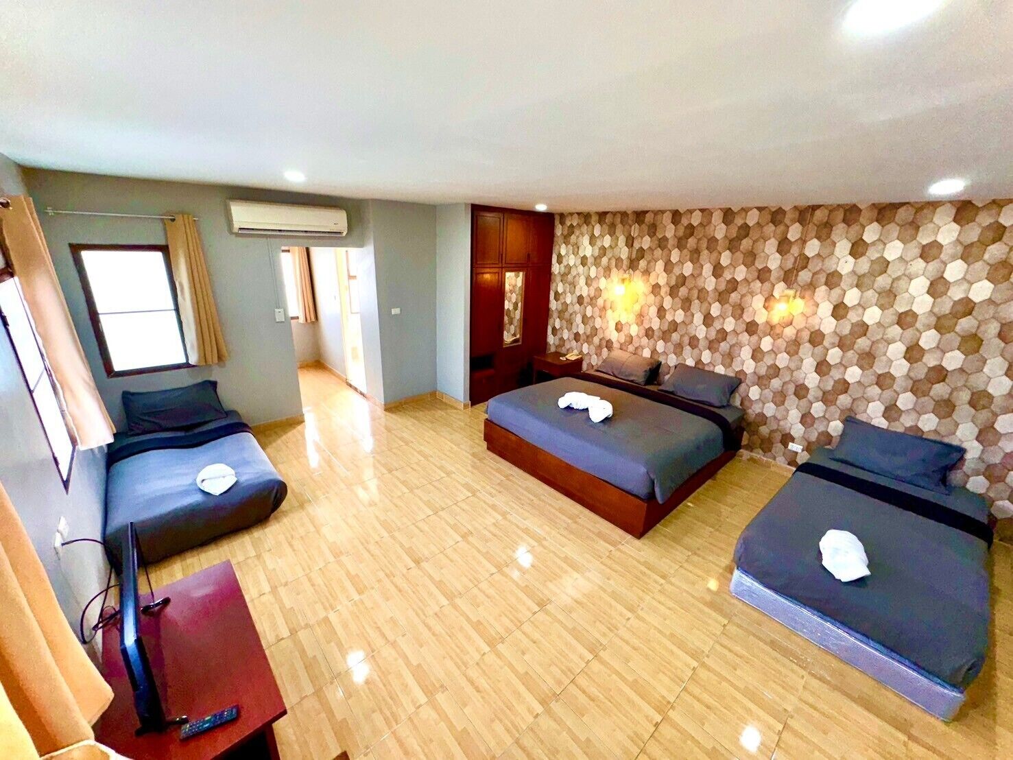 A hotel room with two beds, a TV, and a wooden floor.
