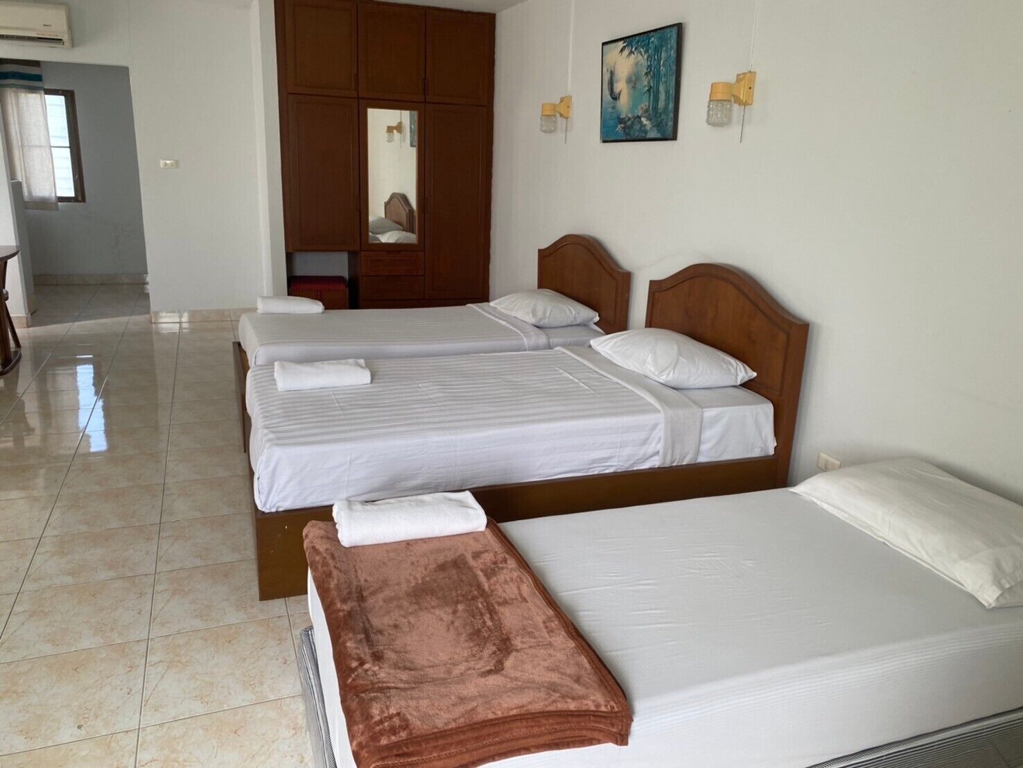 A hotel room with three beds, a wooden wardrobe, a painting on the wall, and a bathroom with a shower.