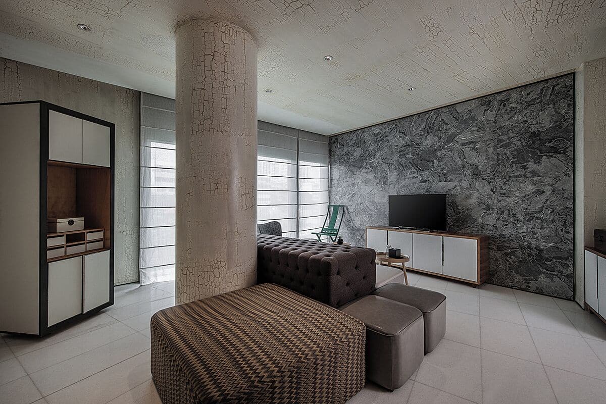 A modern living room with a large window, a television, and a seating area with a patterned ottoman.
