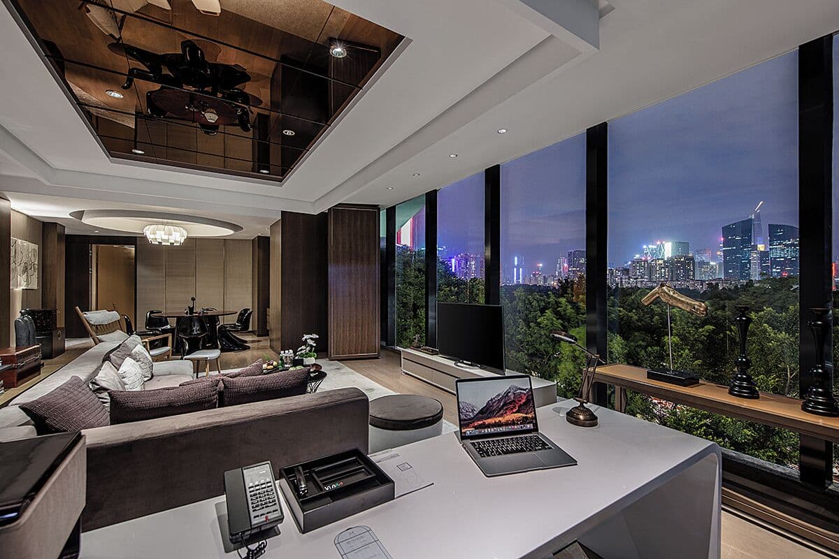 A modern living room with a city view, a sofa, a coffee table, a desk with a laptop, and a television.