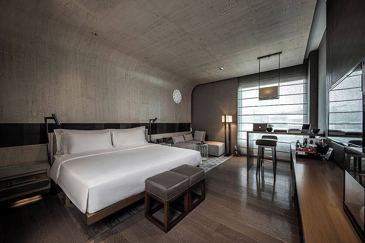 A modern hotel room with a large bed, a desk, and a view of the city.