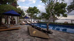 Relax by the pool surrounded by lush greenery and trees, with lounge chairs and umbrellas providing shade.
