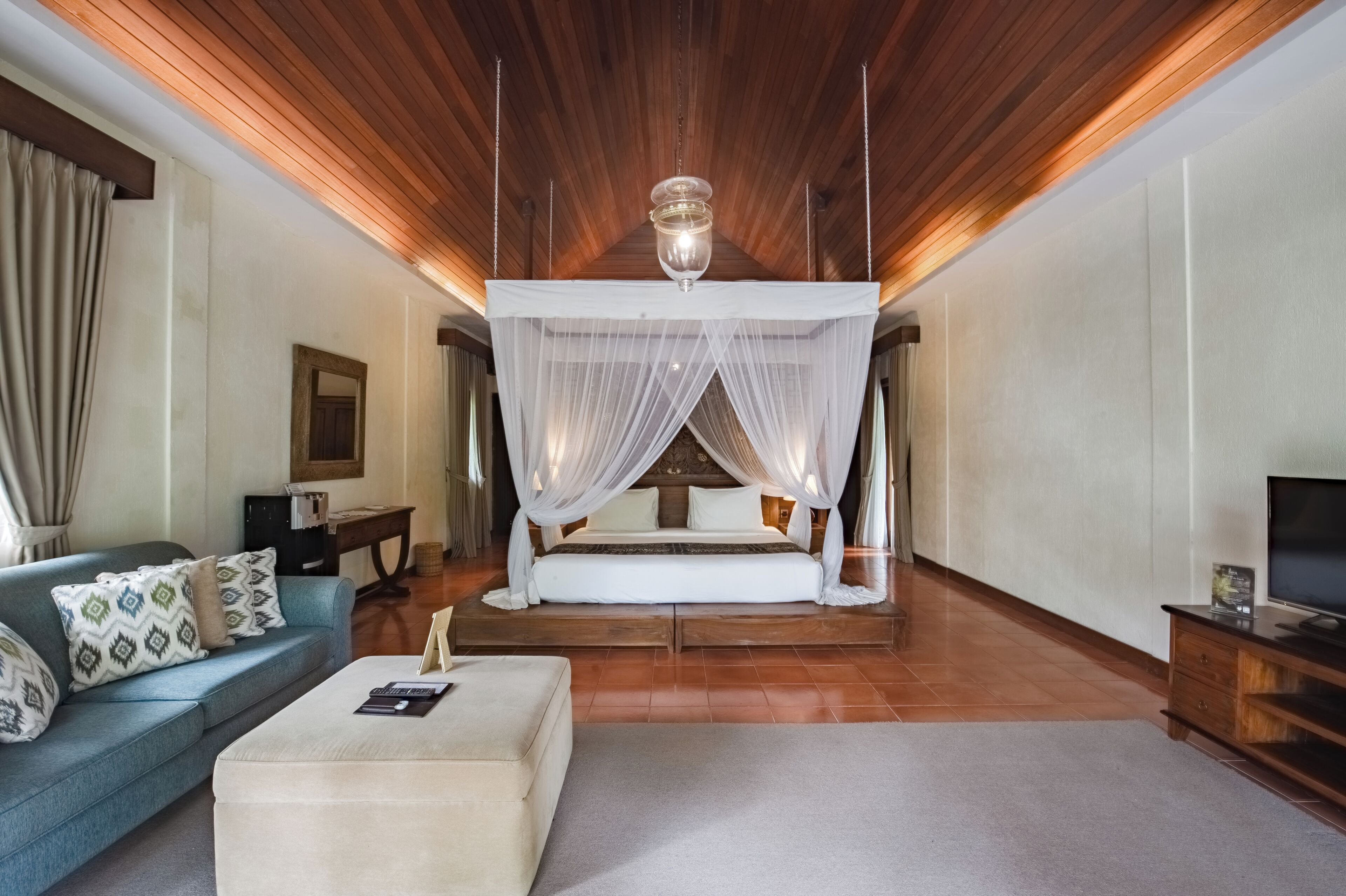 A bedroom with a canopy bed, a sofa, a television, and a wooden ceiling.