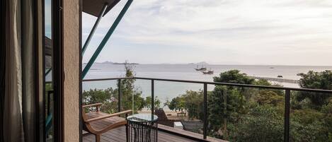 A balcony with a view of the sea, wooden furniture, and a glass table.