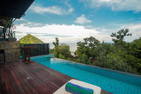 Relax by the serene pool surrounded by lush greenery and a wooden deck.