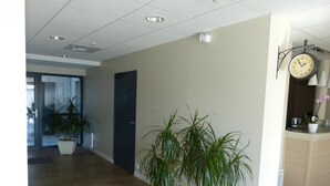 A spacious hallway with wooden flooring, potted plants, a clock, and a door. - Hôtel Terminus (Nantes)