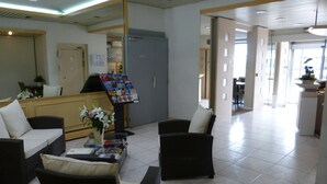 A reception area with a counter, a flower vase, and two sofas. - Hôtel Terminus (Nantes)