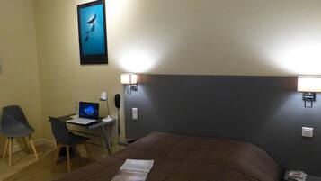 Une chambre d’hôtel comprenant un lit, un bureau avec un ordinateur portable, une chaise et deux lampes fixées au mur.