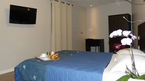 A hotel room with a bed, a flat-screen TV mounted on the wall, a desk, and a potted orchid. - Hôtel Terminus (Nantes)