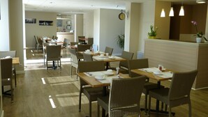 A hotel dining area with wicker chairs, wooden tables, and pendant lighting. - Hôtel Terminus (Nantes)