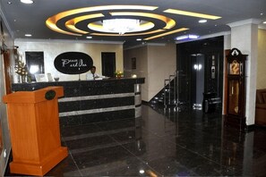 A hotel reception area with a marble counter, a wooden podium, and a chandelier.