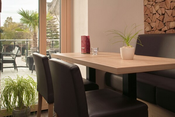 A modern dining area with a wooden table, black chairs, and a potted plant. - Troll's Brauhaus Hotel (Medebach)