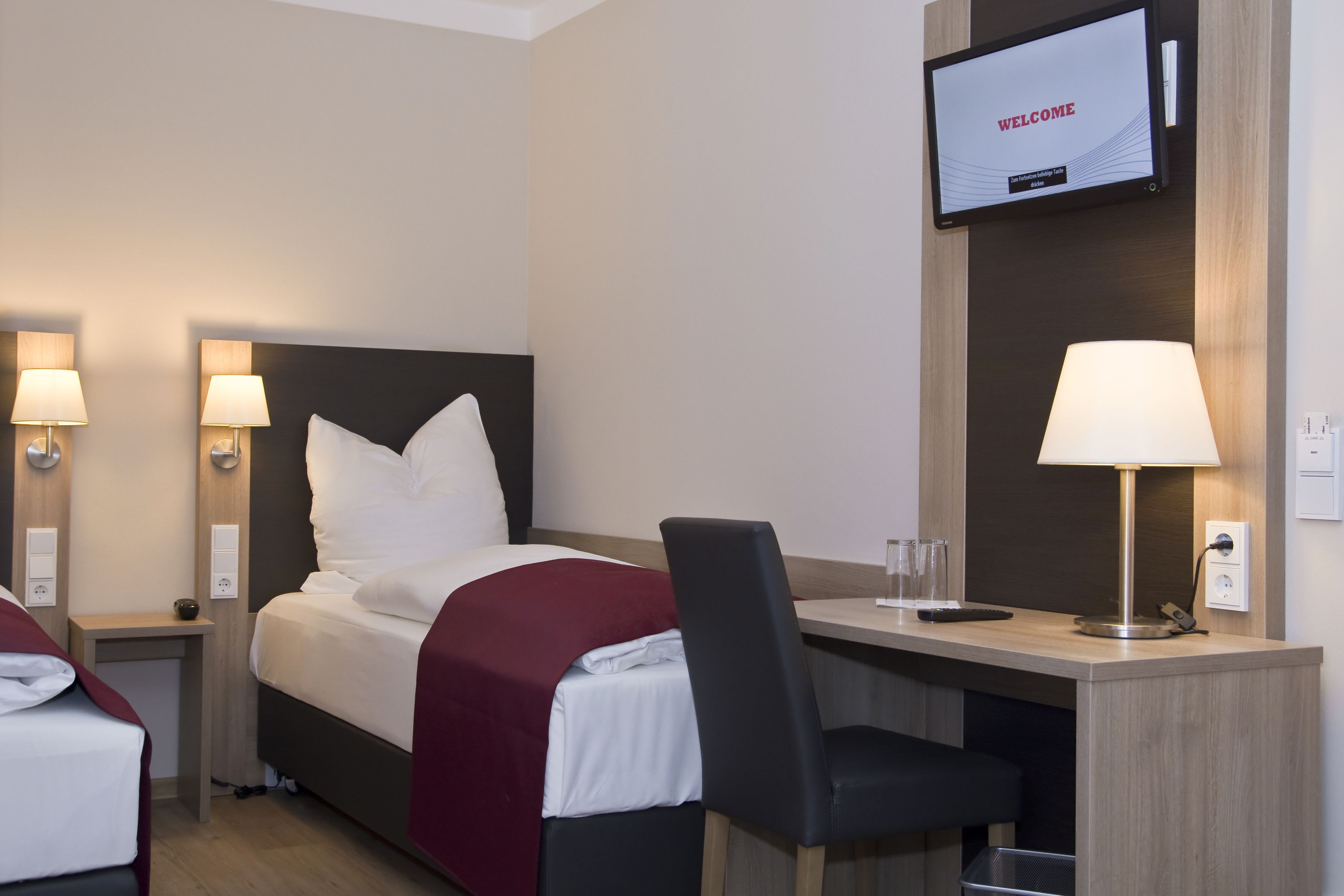 Ein Hotelzimmer mit Bett, Schreibtisch, Stuhl und Fernseher, der "WELCOME" anzeigt.